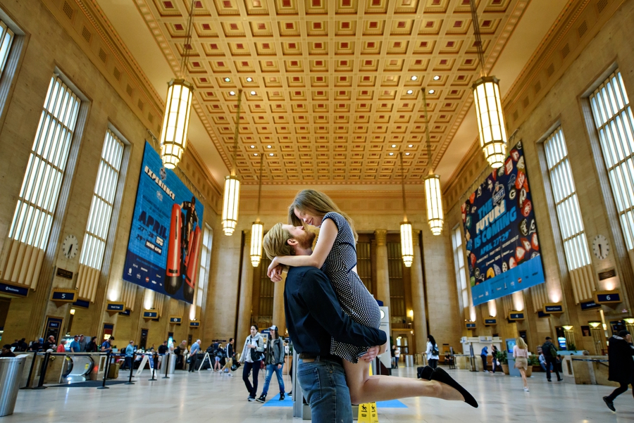A man lifts his fiance up into the air for a kiss at 30th street station.